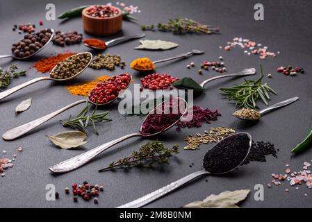 Several types of spices in metal spoons paprika, tomatoes, curry, beets, cumin, turmeric, fennel, spirulina, allspice of different colors on a black c Stock Photo