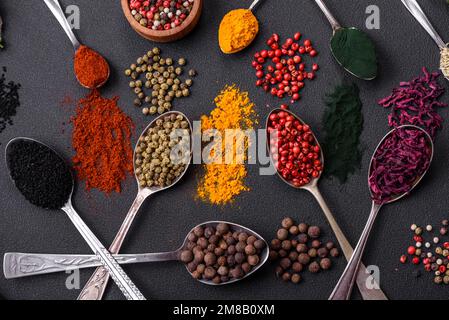 Several types of spices in metal spoons paprika, tomatoes, curry, beets, cumin, turmeric, fennel, spirulina, allspice of different colors on a black c Stock Photo