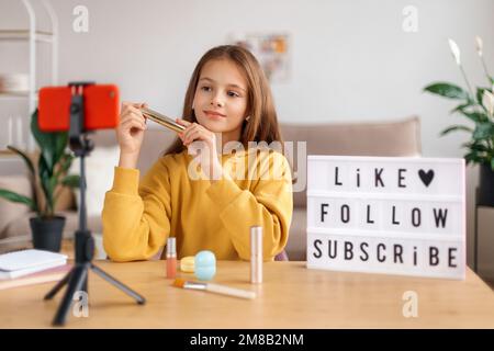 Portrait of young girl vlogger recording video live broadcast on smartphone camera at home. Kid blogger influencer sharing her opinion about cosmetic online with followers via webcam. Social media Stock Photo