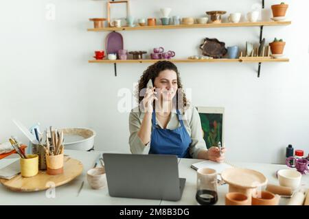 Potter entrepreneur using laptop in workshop, takes orders online Stock Photo