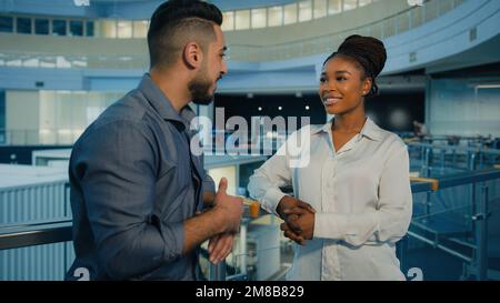 Friendly diverse multiethnic business partners colleagues talking in office hall. African American woman businesswoman and Indian Arabian man Stock Photo