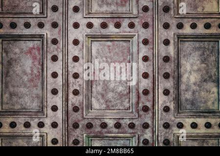 Detail of an ancient paneled door, with painted surface and decorative studs. Vintage background image with space for text. Stock Photo