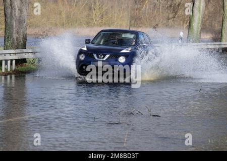 Heuchelheim, Germany. 13th Jan, 2023. A motorist drives over a flooded country road near Heuchelheim in Hesse. Further rainfall could cause more rivers and streams to burst their banks. Credit: Boris Roessler/dpa - ATTENTION: License plate was pixelated/dpa/Alamy Live News Stock Photo
