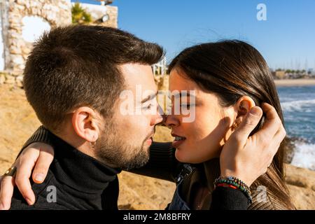 Young man touching hair and kissing girlfriend during romantic shore of waving sea on Saint Valentine Day Stock Photo