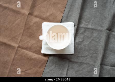 White empty coffee cup on brown and gray fabric background. top view Stock Photo