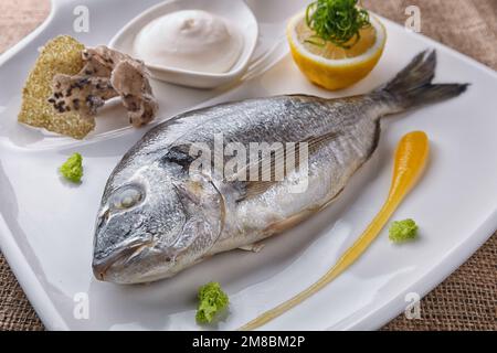 Baked dorado fish with sauce and lemon, on a white plate Stock Photo