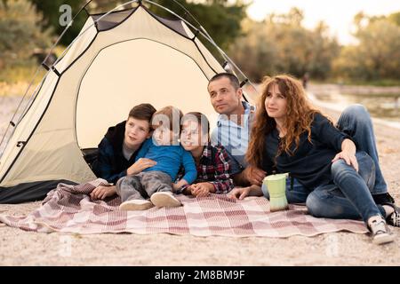 Family resting with tent in nature at summer. Woman, man and children near seaside. Copy space Stock Photo