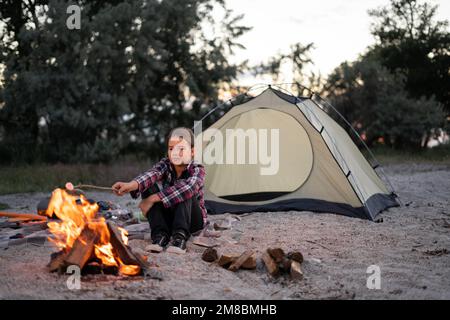 girl roasts marshmallows on a campfire in the evening. Copy space Stock Photo