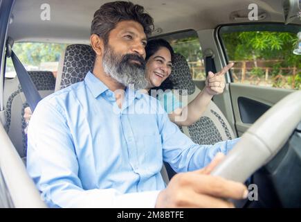 Mature indian man taxi driver driving cab with woman passenger pointing at something on the road. Stock Photo
