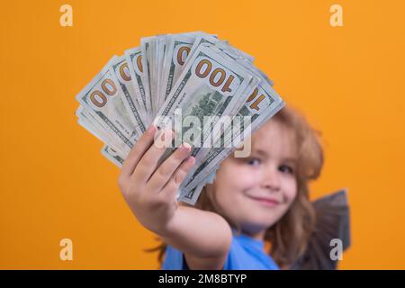 Child with lots of money dollar banknotes isolated over yellow studio background. Stock Photo