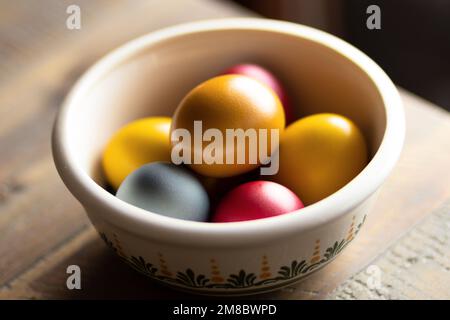 a round bowl with an ornament, in which bright colored Easter eggs lie, stands on a wooden table Stock Photo