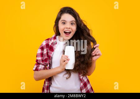Child teen girl with shampoos conditioners and shower gel. Long hair care of teenager. Presenting cosmetic product, shampoo bottle. Amazed teenager Stock Photo