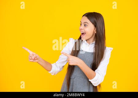 Look at advert. Teenager child points aside shows blank copy space for text promo idea presentation, poses against yellow background. Stock Photo