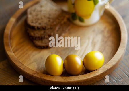 On a round wooden tray are three brightly colored Easter eggs and grain bread. Stock Photo