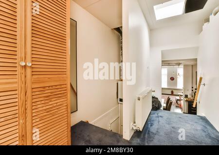 a hallway with wooden shutters on the wall and blue carpeted flooring in front of the door to the room is white Stock Photo