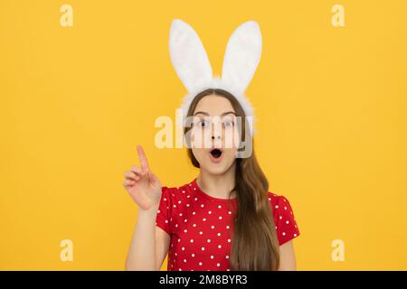 Teen girl wearing bunny ears isolated at yellow background. Amazed surprised emotions of young teenager girl. Stock Photo