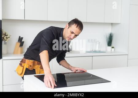 Man electrical repairs kitchen surface apartment. Installing hob in countertop. Man bought new kitchen furniture and appliances. Process installing an Stock Photo