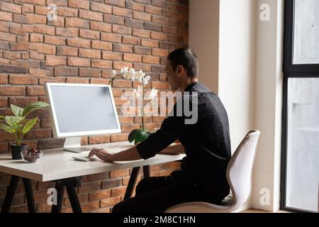 Focused young man using laptop, typing on keyboard, writing email or message, chatting, shopping, successful freelancer working online on computer. Stock Photo