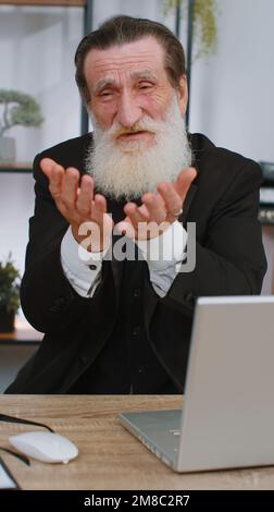 Conflict, quarrel, negotiation. Angry senior businessman ceo making conversation with colleague at home office workplace. Upset mad freelancer grandfather old man talking, looking at camera indoors Stock Photo