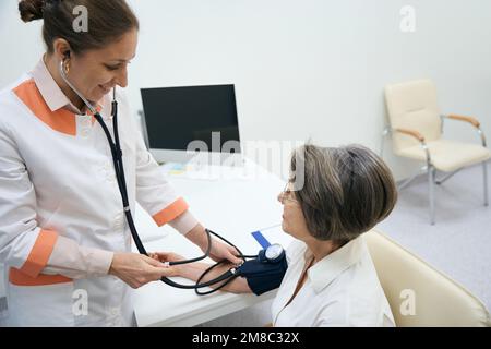 Smiling therapist measures the blood pressure of patient with tonometer Stock Photo