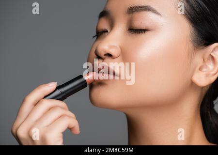 Young asian woman with makeup applying lipstick isolated on grey,stock image Stock Photo