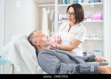 Cosmetologist uses fillers for a rejuvenating course for elderly man Stock Photo