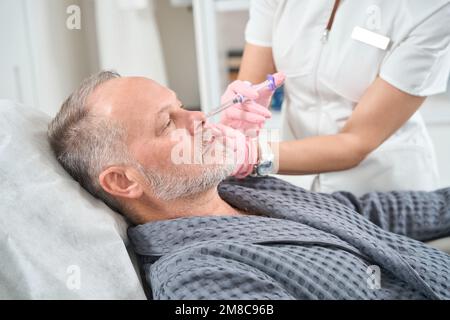 Doctor uses modern fillers for rejuvenating course for elderly patient Stock Photo