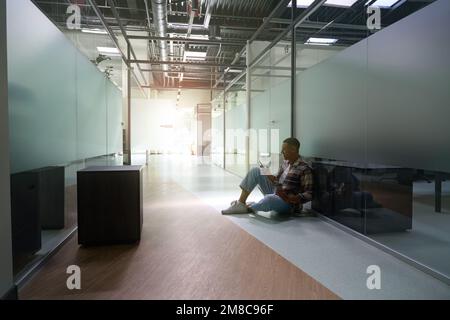 African American man sitting on the floor and typing a message on the phone Stock Photo