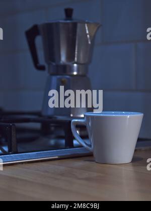 Moka pot on kitchen stove with coffee mug on worktop Stock Photo