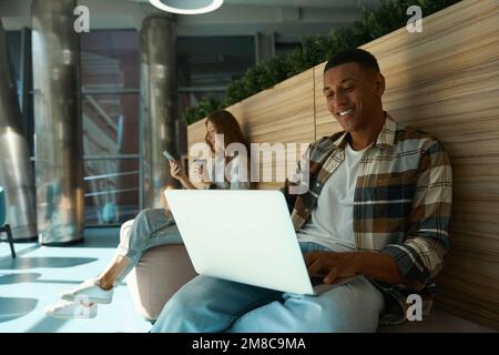 Happy African American guy typing on laptop in office hall Stock Photo