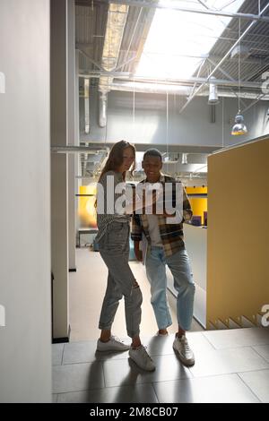 Two friends looking at phone screen while standing in the office hall Stock Photo