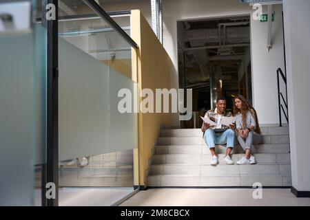 Smiling man and lady sitting on steps and examining the documents Stock Photo