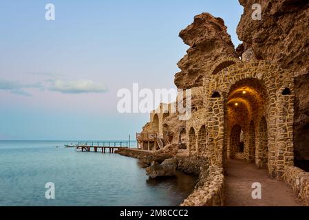 Stone carved corridor by red sea beach with a jetty at the horizon - dusk Stock Photo