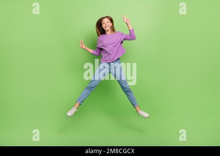 Full length photo of cheerful satisfied cute girl straight hairdo wear purple pullover showing v-sign isolated on green color background Stock Photo