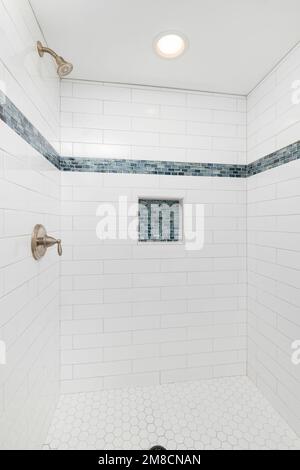 A shower with white and blue subway tiles, bronze faucet, and a white hexagon tile floor. Stock Photo