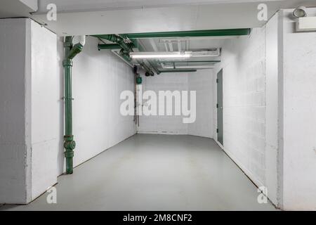An empty parking garage spot with white walls, green pipes, and concrete floor. Stock Photo