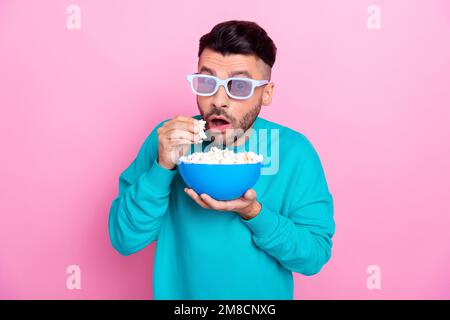 Photo of funny young student wearing blue pullover eating careful silent his popcorn wear glasses cinema hall isolated on pink color background Stock Photo