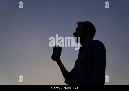 Male person in silhouette outdoor drinking coffee or tea at sunset. Adorable dusk at background. High quality image Stock Photo