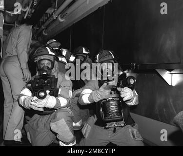 Wearing protective suits and oxygen breathing apparatuses (OBAs), the members of two hose teams wait to advance down a passageway during a firefighting drill aboard the nuclear-powered aircraft carrier USS ABRAHAM LINCOLN (CVN-72). The LINCOLN's crew is receiving refresher training under the supervision of personnel from Fleet Training Group, Guantanamo Bay, Cuba. Country: Caribbean Sea Stock Photo