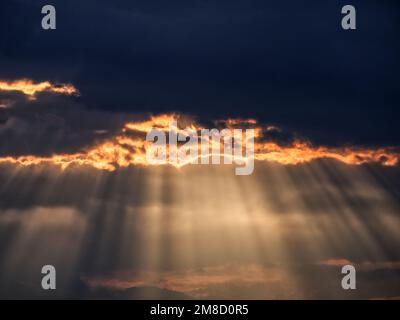 A scenic shot of sunbeams poking through fiery clouds at sunset, perfect for background Stock Photo