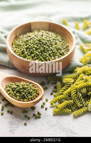 Mung bean fusilli pasta on a gray concrete background. Bowl with raw pasta and green mung bean. Gluten free pasta. Stock Photo