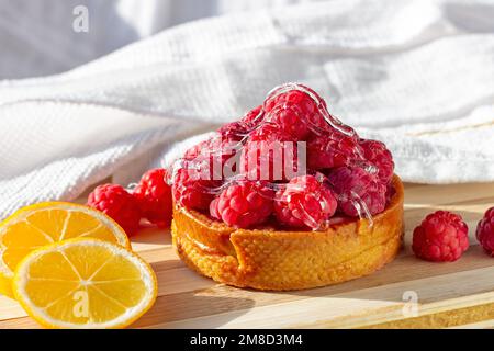 Pink fresh raspberry tart and fresh lemons on the kitchen table background. Stock Photo