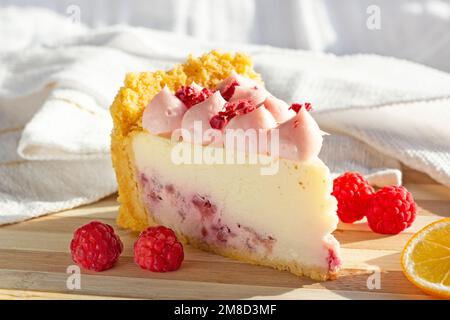 Delicious white and pink sweet raspberry cheesecake slice with fresh berries on the wooden board in the kitchen. Stock Photo