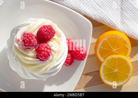 Top view of white mini meringue Pavlova cake with sweet pink raspberry berries and mascarpone cream on the plate in the kitchen. Stock Photo