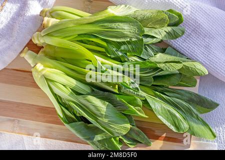 Top view of raw green Chinese cabbage pak choi or bok choy baby vegetables on the wooden board in the kitchen. Stock Photo