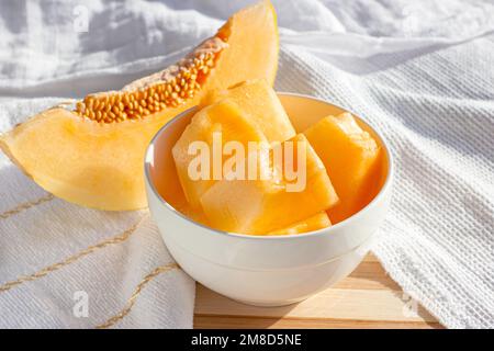 Fresh sweet juicy honey melon (cantaloupe) slices in a white bowl in the kitchen in summer. Stock Photo