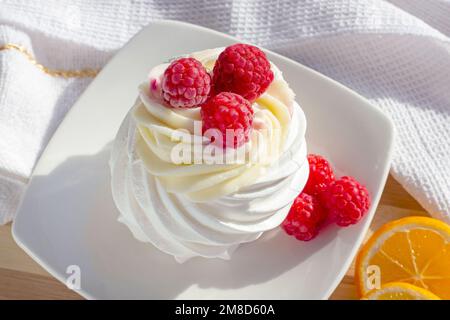 White mini meringue Pavlova cake with sweet pink raspberry berries and mascarpone cream on the plate in the kitchen. Stock Photo