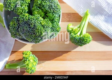Top view of bright green organic raw broccoli  branches in the white bowl on the table in the kitchen close up with copy space. Stock Photo