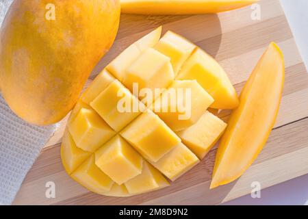 Top view of bright yellow cube sliced fresh mango on wooden cutting board close up. Stock Photo