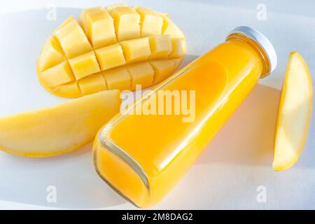 Bright yellow mango juice in a glass bottle with sliced fresh mangos on white background close up. Stock Photo
